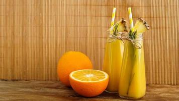 zwei Flaschen tropischer Saft mit Papierstrohhalmen. Orangen und Ananas foto
