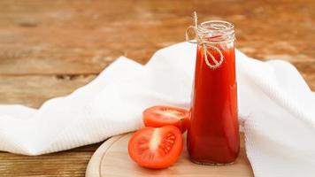 Tomatensaft in Glasflasche und frische Tomaten auf Holzuntergrund