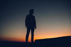 Silhouette eines Mannes, der den Sonnenuntergang über der Stadt beobachtet foto