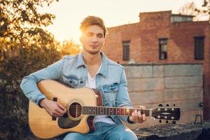 junger Mann, der Gitarre in der Stadt auf Sonnenstrahlenhintergrund spielt foto
