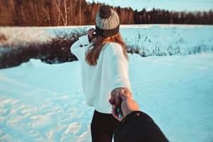 Folgen Sie mir Mädchen, das die Hand des Freundes im Winterschneewald hält. foto