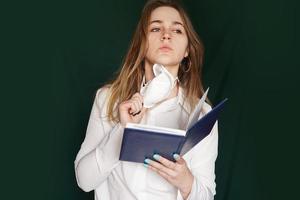 junges Mädchen in einer medizinischen Maske in einer weißen Bürobluse mit einem Notebook foto