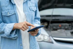 abbauen, gebrochen Auto, Reparatur. Frau Verwendet Handy, Mobiltelefon Telefon prüfen Versicherung Prämien durch Anwendung fällig zu Auto Unfall . finden Garage zu erhalten Auto Fest während Land Tour, warten zum Hilfe, Notfall foto