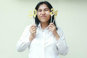 asiatisch Büro Arbeiter jung Frau aufgeregt zu feiern 2024 Neu Jahre Vorabend durch halten Ziffer glänzend golden Kerzen tragen Weiß formal passen suchen Weg isoliert foto