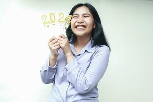 aufgeregt asiatisch jung weiblich Mitarbeiter lächelnd und suchen Seite mit halten Zahl golden Kerzen zum 2024 Neu Jahre Vorabend Feier tragen grau formal passen isoliert foto