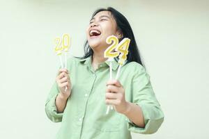 sorglos asiatisch jung Frau Lachen und suchen Weg tragen Grün Übergröße Hemd mit erziehen Arm zeigen 2024 Zahl Kerzen zu Kamera, isoliert, weiblich feiern Neu Jahre Vorabend foto