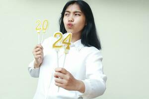 nachdenklich asiatisch jung Geschäft Frau zeigen Nummer 20 und 24 Zahl Kerzen während suchen Weg mit küssen Lippen tragen fromal Weiß Shirt, Neu Jahre Vorabend Konzept, isoliert foto