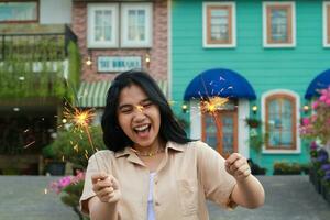 heiter jung asiatisch Frau halten Wunderkerze zu feiern Neu Jahr Vorabend mit Garten Party Stehen Über bunt Jahrgang Haus Hof foto