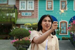 Neu Jahr Vorabend Feier Konzept. attraktiv asiatisch jung Frau halten Wunderkerze mit Lachen glücklich im draussen Garten von Jahrgang Haus Hof foto