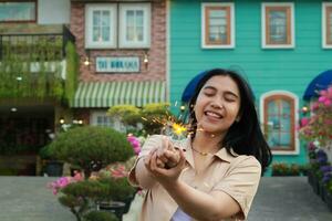 Neu Jahr Vorabend Feier Konzept. attraktiv asiatisch jung Frau halten Wunderkerze mit Lachen glücklich im draussen Garten von Jahrgang Haus Hof foto