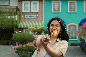 Neu Jahr Vorabend Feier Konzept. attraktiv asiatisch jung Frau halten Wunderkerze mit Lachen glücklich im draussen Garten von Jahrgang Haus Hof foto