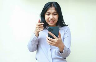 schön asiatisch jung Frau wütend mit Handy, Mobiltelefon Telefon zeigen mit Zeigefinger zu Bildschirm tragen formal passen isoliert auf Weiß Hintergrund foto