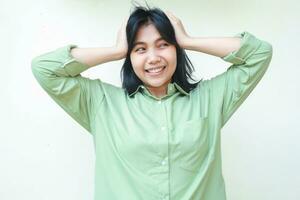 Nein Weg. lächelnd asiatisch Frau tragen Grün Über Größe Hemd greifen ihr Kopf und suchen Weg sehen etwas unglaublich während Stehen Über isoliert Weiß Hintergrund foto
