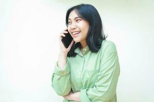 begeistert erfolgreich asiatisch Frau tragen Grün Übergröße Hemd reden auf Smartphone Lachen von komisch Konversation Stehen Über isoliert Weiß Hintergrund foto