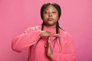wütend Frau tun Auszeit Geste mit t gestalten Hände Herstellung brechen Zeit Zeichen mit Waffen im Studio mit Rosa Hintergrund. afrikanisch amerikanisch jung Erwachsene Werbung Pause Symbol mit Palmen foto