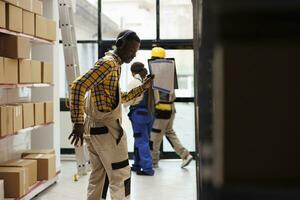 Warenhaus Supervisor halten Papiere Zwischenablage und Tanzen im Lager. afrikanisch amerikanisch Lagerhaus operativ tragen haufenweise, Hören zu Musik- und Herstellung Bewegungen beim Arbeit foto