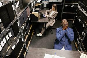 oben Aussicht von Manager mit nachdenklich Ausdruck, Brainstorming Ideen zu lösen Bürokratie Bericht im Lager Zimmer. vielfältig Geschäft Menschen Arbeiten im Laufe der Zeit beim administrative Forschung foto