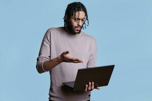 verwirrt arabisch Mann erklären Geschäft planen zu Kunde im online Treffen auf Laptop. gereizt jung Person halten tragbar Computer und haben Konversation im Video Anruf foto