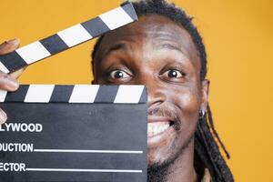 Porträt von Mann halten Tafel zu Schnitt Szenen im Film Industrie, posieren auf Gelb Hintergrund. afrikanisch amerikanisch jung Erwachsene Arbeiten im Film Herstellung Produktion und Kinematographie foto