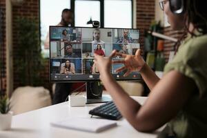 afrikanisch amerikanisch Anfang Mitarbeiter Arbeiten von Zuhause gestikulieren im Video Konferenz mit Kollegen beim Schreibtisch. klein Geschäft Inhaber reden mit Mannschaft im Internet Anruf auf persönlich Computer mit Webcam. foto