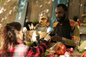 afrikanisch amerikanisch Mann zeigen natürlich gesund Produkte von Bauern Markt Stand, örtlich gewachsen Lebensmittel. männlich Farmer reden zu Kunde Über verschiedene saisonal organisch Vegetarisch Produkte. foto