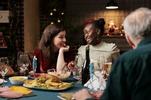 vielfältig freunde Treffen auf Weihnachten zum Abendessen, feiern Dezember Urlaub beim heim. Menschen genießen Feier beim Tabelle umgeben durch festlich Dekorationen und Weihnachten Baum, Gefühl glücklich. foto