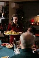 Frau Putten festlich Essen auf Tisch, genießen Weihnachten Abendessen und saisonal Feier mit vielfältig freunde und Familie beim heim. Menschen Gefühl glücklich Essen hausgemacht Mahlzeit und Trinken Alkohol. foto
