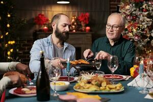 vielfältig Menschen Versammlung um Tabelle zu feiern festlich Winter Urlaub, Gefühl glücklich während Weihnachten Vorabend Abendessen. freunde und Familie genießen Zeit beim Zuhause mit traditionell hausgemacht Lebensmittel. foto