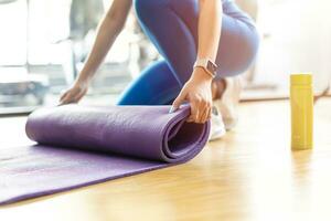 Yoga Matte. Nahansicht Frauen Hände ist rollen tpe Gummi Übung Fitness Yoga Matte auf das Fußboden beim Sport Verein. foto