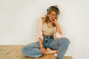 attraktiv Frau mit Vergnügen Hören Lieblings Musik- während Sitzung auf das Fußboden im ihr Leben Zimmer. Weiß Hintergrund. foto