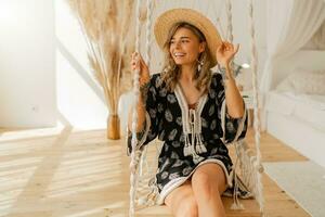 gemütlich Zuhause Atmosphäre. schön stilvoll blond Frau im Boho Kleid posieren im stilvoll Schlafzimmer. foto