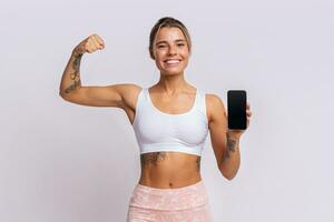 Ausbildung App. passen ziemlich Frau zeigen Smartphone mit modern Fitness Anwendung zum Verfolgung Sport Aktivität. posieren Über Gelb Studio Hintergrund. foto
