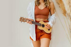 Frau spielen Ukulele Gitarre Über Weiß Hintergrund im Studio mit Pampas Gras Dekor. Einzelheiten. foto