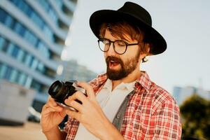 verlassen Mann mit Bart mit interessant mit retro Film Kamera , Herstellung Fotos. Tourist Mähne Gehen im groß modern Stadt. foto