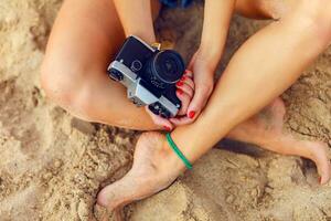 jung Dame Sitzung auf das tropisch warm Strand ein halten retro Kamera.Hände Nahaufnahme. foto