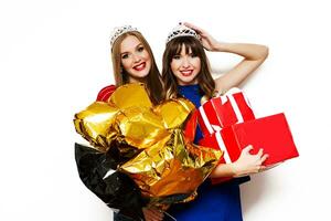 Innen- Lebensstil positiv Porträt von zwei ziemlich Frauen, Beste freunde mit hell Party Luftballons, Maskerade Kronen posieren auf Weiß Hintergrund.holding groß rot Geschenk Kasten. foto