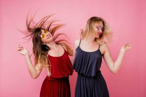 zwei sorglos weiblich haben Spaß und Tanzen auf Rosa Hintergrund. Blitz Porträt. Party Stimmung . ähnlich Kleid. Freundschaft Konzept. foto