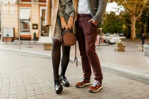 Mode Einzelheiten. stilvoll elegant Mann mit Frau posieren draussen im sonnig Frühling Tag. modisch Paar im Liebe. tragen Schuhe und Turnschuhe. Hand Tasche. Beige Mantel . foto