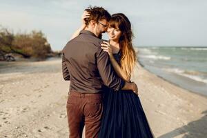 zwei glücklich Menschen im Liebe, elegant Frau mit ihr gut aussehend Freund umarmen und genießen romantisch Zeit zusammen auf das Strand. elegant Kleid. foto