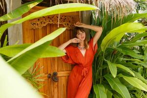Herrlich Brünette Frau im stilvoll Sommer- Outfit genießen Ferien im Luxus Erholungsort. exotisch Garten mit tropisch Pflanzen. foto