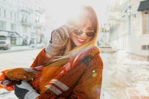 wunderbar glücklich Frau im stilvoll Schal und flauschige Jacke genießen Winter Ferien im sonnig europäisch Stadt. foto