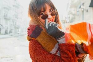 wunderbar glücklich Frau im stilvoll Schal und flauschige Jacke genießen Winter Ferien im sonnig europäisch Stadt. foto