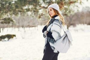 Winter Lebensstil Porträt von jung blond frisch Dame im warm wolle flauschige Schal und Hut mit Rucksack Gehen im wunderbar Winter Park. foto