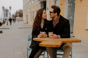modisch Paar im Liebe Sitzung im Straße Cafe und Trinken heiß Kaffee während Reisen im Europa. foto