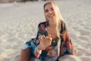 Sommer- Lebensstil Bild von blond Frau Zeichnung Aquarell Blume durch Bürste. Künstler Sitzung auf das Strand. Bohemien Outfit. foto