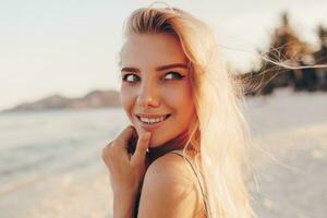 Sommer- Lebensstil Bild von blond Frau Zeichnung Aquarell Blume durch Bürste. Künstler Sitzung auf das Strand. Bohemien Outfit. foto