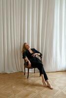 Innen- Studio Foto von elegant blond Frau Sitzung auf das Stuhl. beiläufig Mode sehen. Eleganz, verführerisch Stimmung.