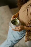 Lebensstil Foto von ziemlich Brünette Frau im modisch Ernte oben und Blau Jeans halten Tasse von Kaffee. modern Innere.