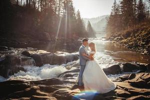 Hochzeitspaar auf einem Berg- und Flusshintergrund in den Sonnenuntergängen foto