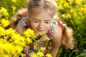 Kleines blondes Mädchen atmet Blumenduft ein foto